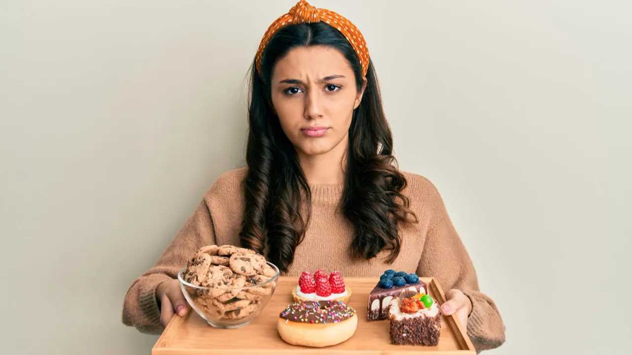 Mujer preocupada con dulces, reflejando ansiedad por comer en exceso.