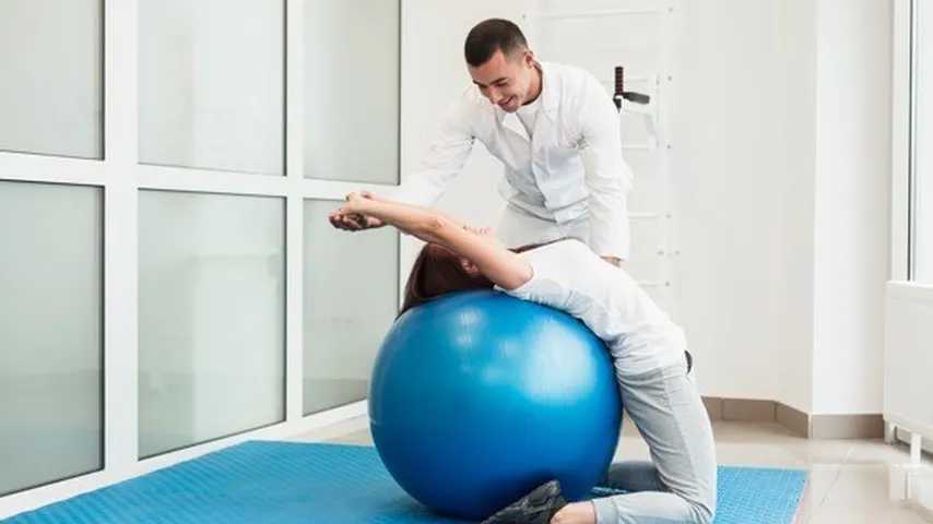 Médico con una paciente haciendo ejercicios de estiramientos con una pelota. (Foto: Freepik)